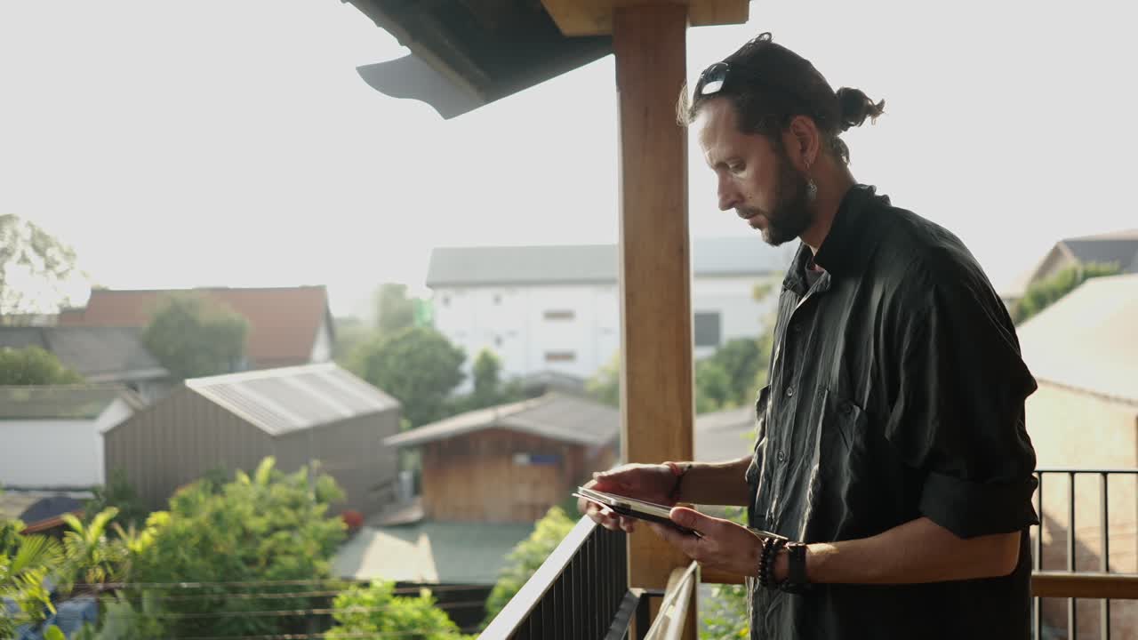 A man on a modern balcony enjoying the view and using a tablet