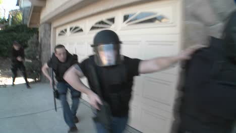 dea or swat officers with arms drawn perform a drug raid on a house