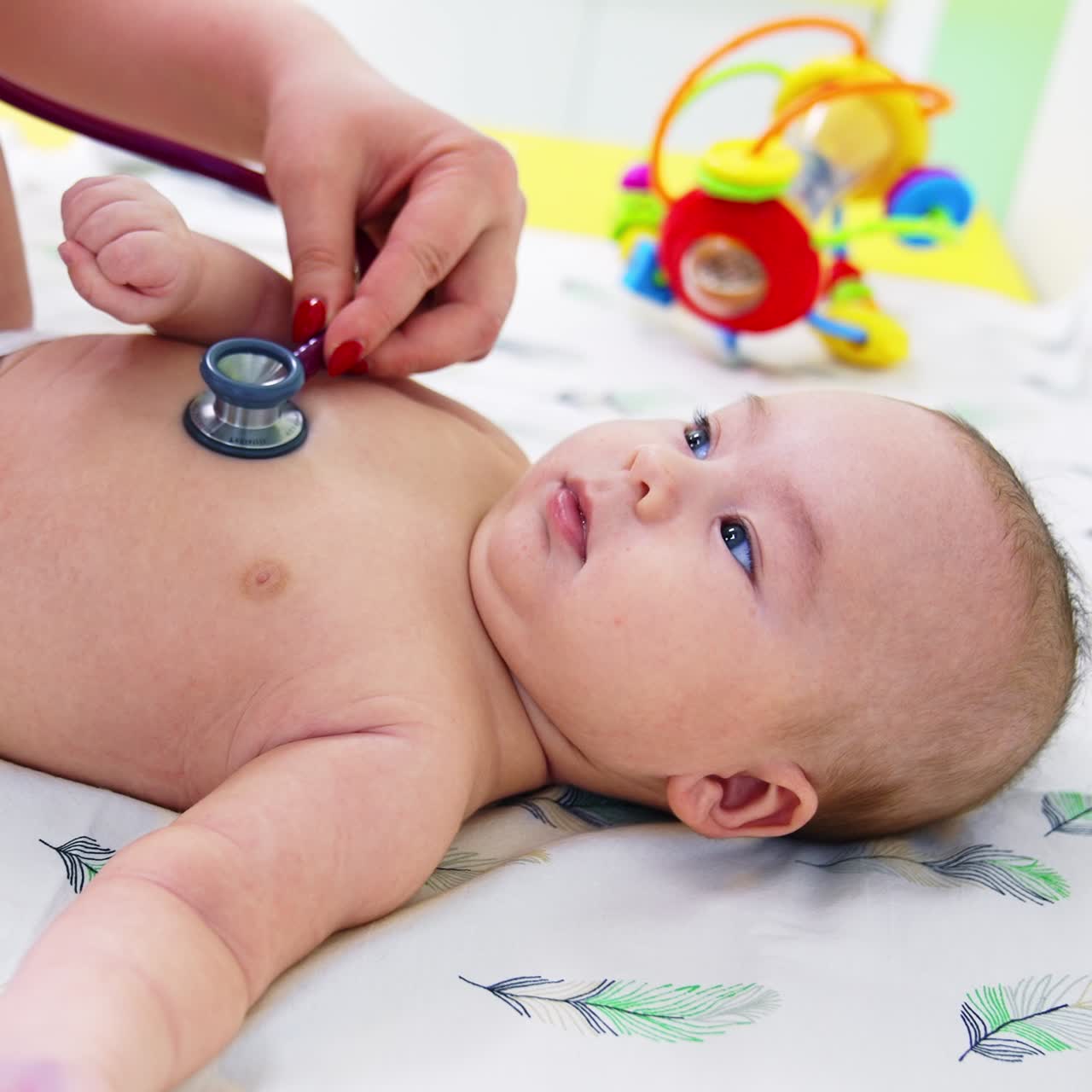 Doctor's hand puts stethoscope on baby boy's chest. Calm beautiful kid lying peacefully on the pediatrician's table. Close up