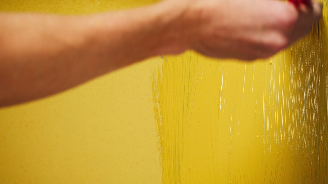 Primo piano di una mano che dipinge una parete con vernice gialla