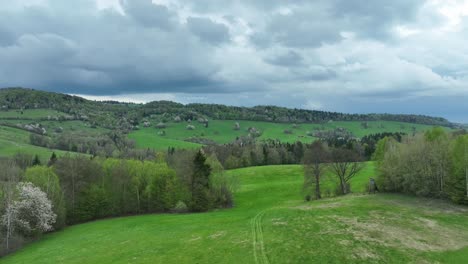 explore el esplendor de la primavera mientras el dron se eleva bajo sobre los huertos y prados en flor, revelando un sinuoso camino sin pavimentar y todo debajo de un lienzo de nubes dramáticas y cielos azules