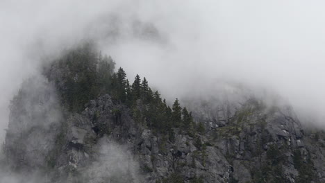 mist gently rolling over forest trees on mountain cliff in british columbia, aerial