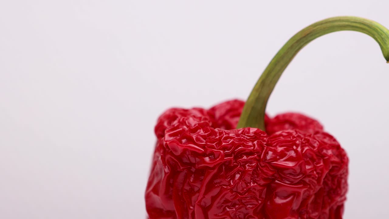 녹색 줄기가 회전하는 주름진 생생한 붉은 파프리카의 윗부분은 지나치게 익은 채소의 오래된 껍질을 시들게 하는 복잡한 세부 사항과 질감을 보여줍니다.