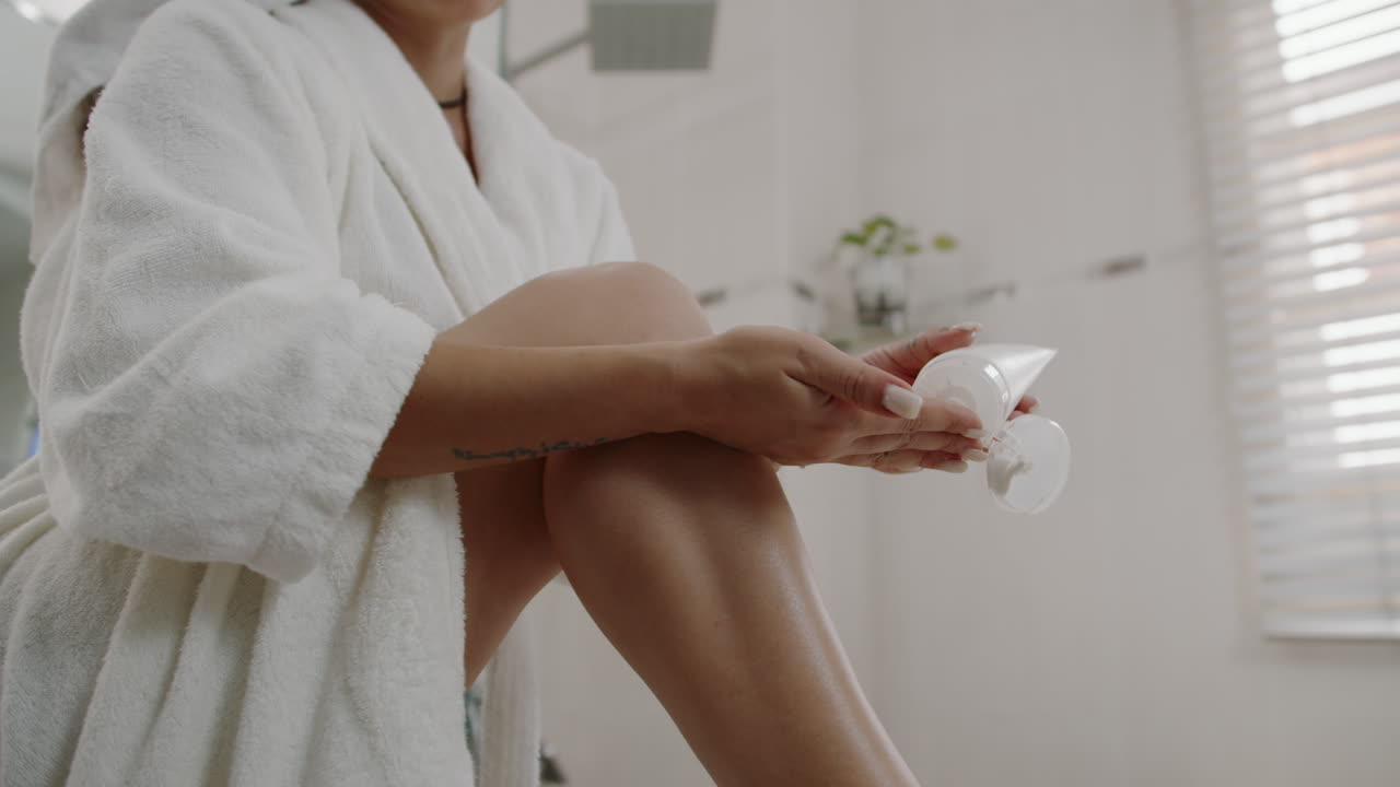 Oigenkännlig kvinna smörjer in benen med lotion efter badet