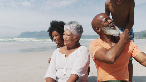 Porträt-Eines-älteren-Paares-Gemischter-Abstammung-Mit-Enkelkindern,-Die-Am-Strand-Spielen-Und-Lächeln