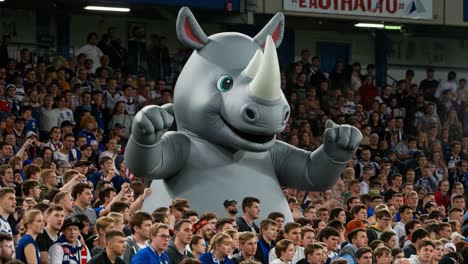 a giant inflatable rhinoceros cheers enthusiastically among excited spectators at a lively sporting event, capturing the vibrant atmosphere of fan engagement and team spirit