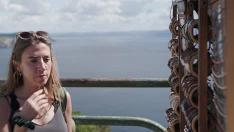 young woman with backlight at a craft kiosk buying bracelets, with the ocean in the background