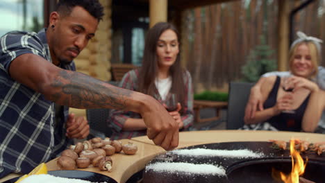 smiling friends relaxing on grill party outdoors. man putting salt on bbq grill