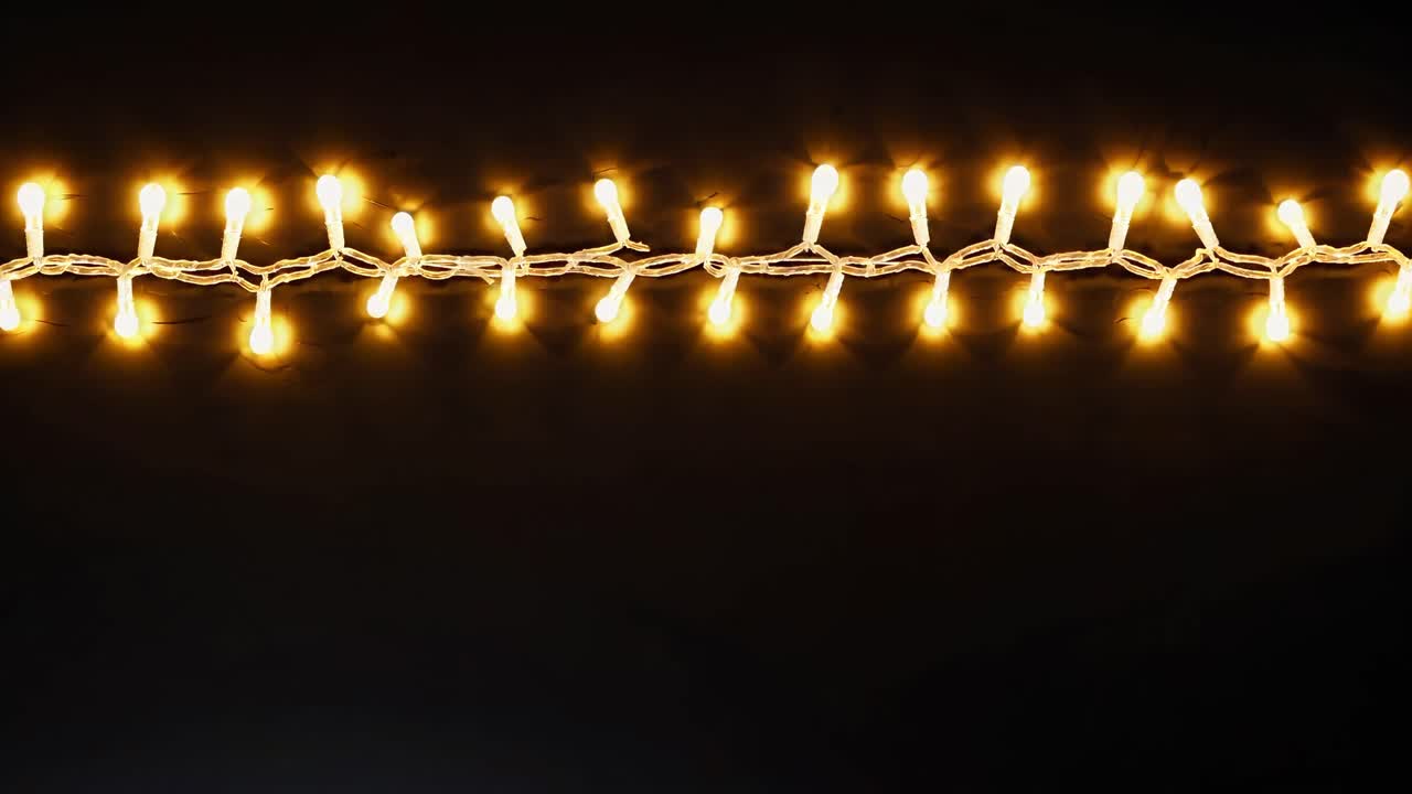 Close-up, horizontal angle of glowing string lights against a dark background, ideal for festive