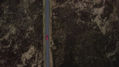 Bird-eye-view-of-a-red-vehicle-travelling-along-a-single-track-road,-aerial