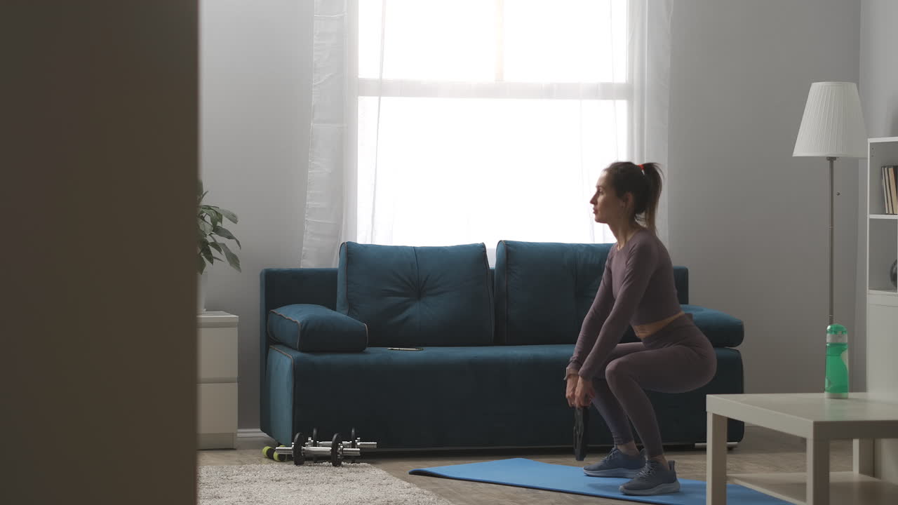 donna sexy con coda di cavallo sta facendo squat con il peso nelle mani allenamento dei muscoli dei glutei e delle gambe esercizi di fitness a casa a lungo tiro in appartamento