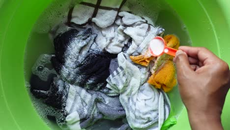 washing clothes in a green bucket with detergent