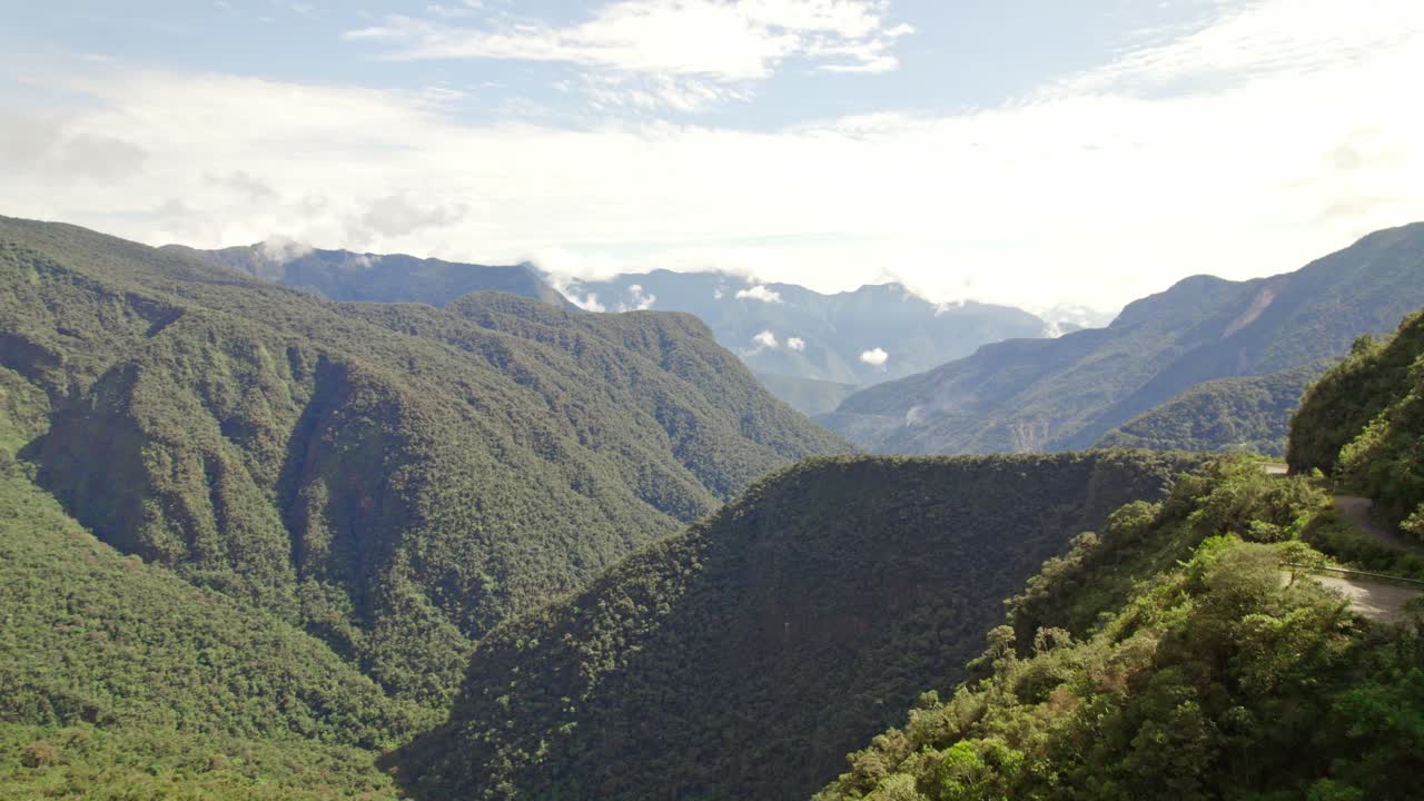 The notorious Death Road in the Bolivian Andes. The video highlights the narrow, unpaved road cut into the steep, heavily vegetated cliff face, famous for mountain biking and extreme travel