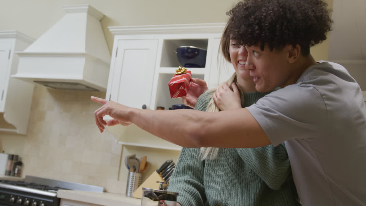 una pareja feliz y diversa sonriendo con regalos en casa juntos