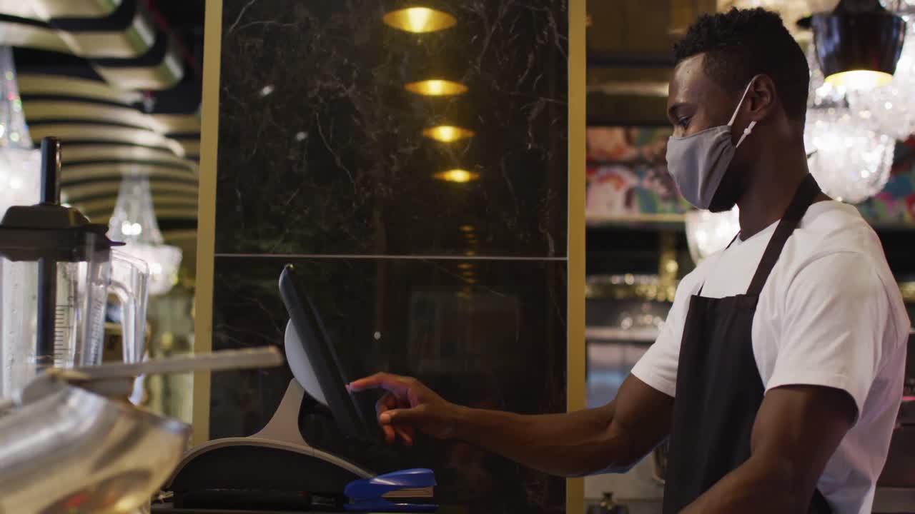 African american male barista wearing face mask using till