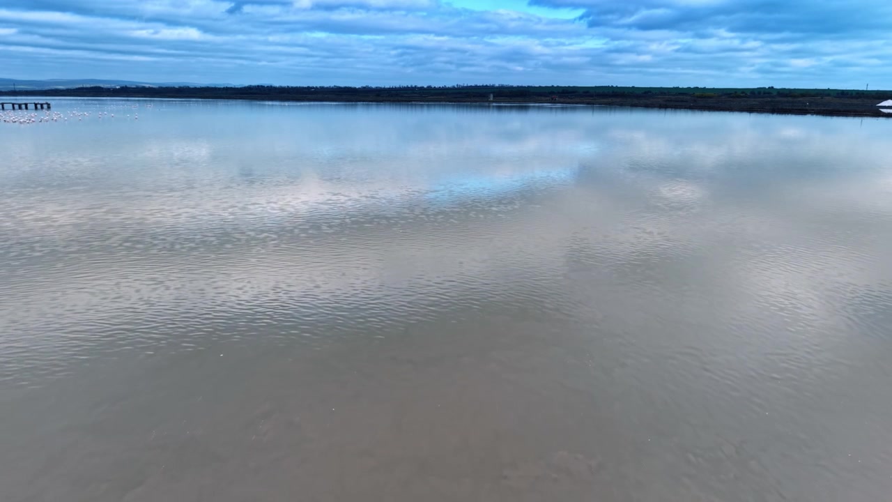 L'acqua riflette le nuvole nel lago calmo nel tardo pomeriggio, vicino alla campagna. L'acqua del lago mostra il cielo e le nuvole mentre il sole inizia a tramontare nell'area rurale