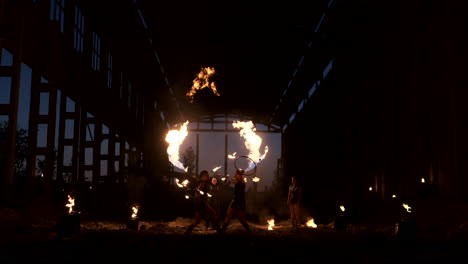 four women in leather clothes with fire dance and show fire show a man with a flamethrower in the back plays with the flame in slow motion