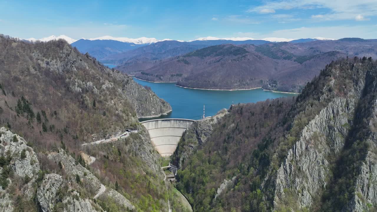 A dam nestled between mountains with a scenic lake and distant hills in the background, aerial view