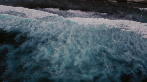 Aerial-birds-eye-view-of-dramatic-dark-moody-ocean-water-with-white-foaming-waves-breaking