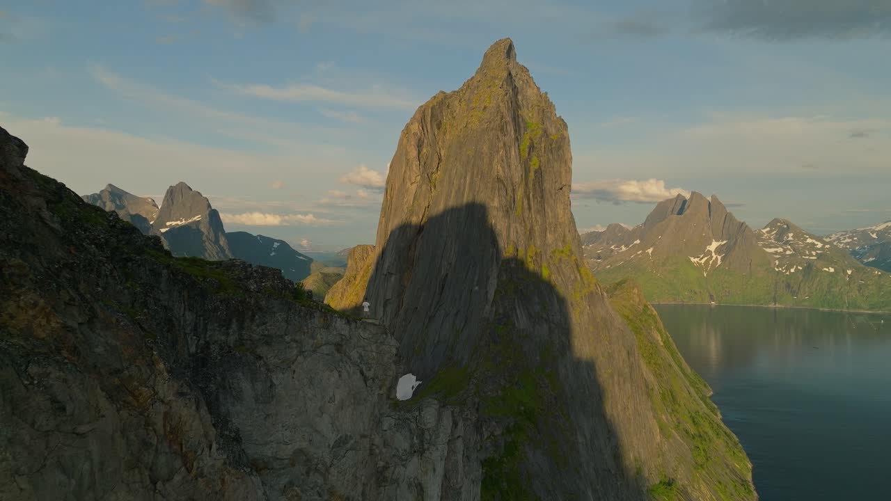 Persona in piedi su una roccia di fronte all'iconica cima del monte Segla sull'isola di Senja, Norvegia, sulla vetta dell'escursione Hesten. Un drone sorvola rivelando le scogliere a picco che emergono dall'acqua.