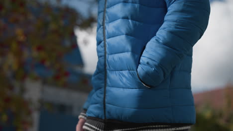 close-up of an individual in blue jacket holding a shopping bag, focused on the hand and pocket strolling, detail against a blurred outdoor background