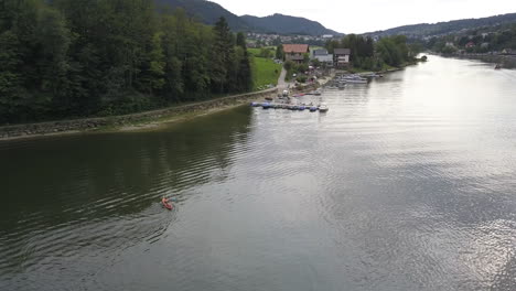 A-small-boat-is-navigating-on-a-flat-stream-near-the-shore-with-fir-forest,-river-in-Switzerland:-Doubs