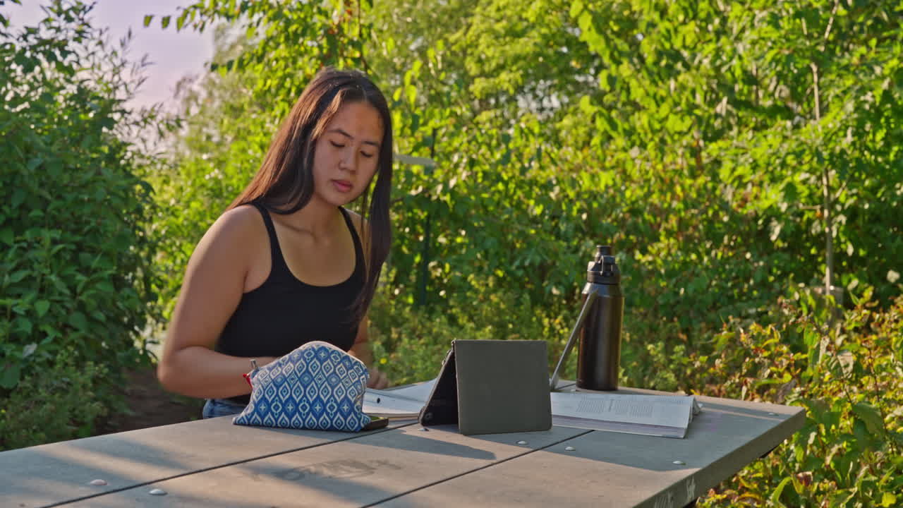 Ethnically ambiguous female outdoor studying for school in an outdoor park setting on a sunny afternoon