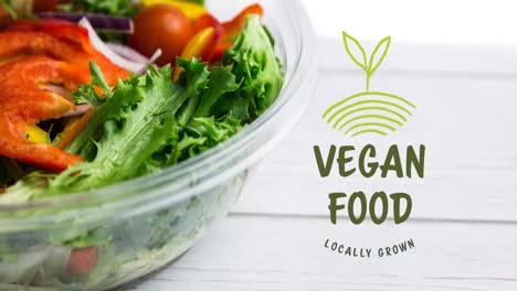 animation of vegan food text in green over fresh organic vegetable salad in bowl on wooden boards