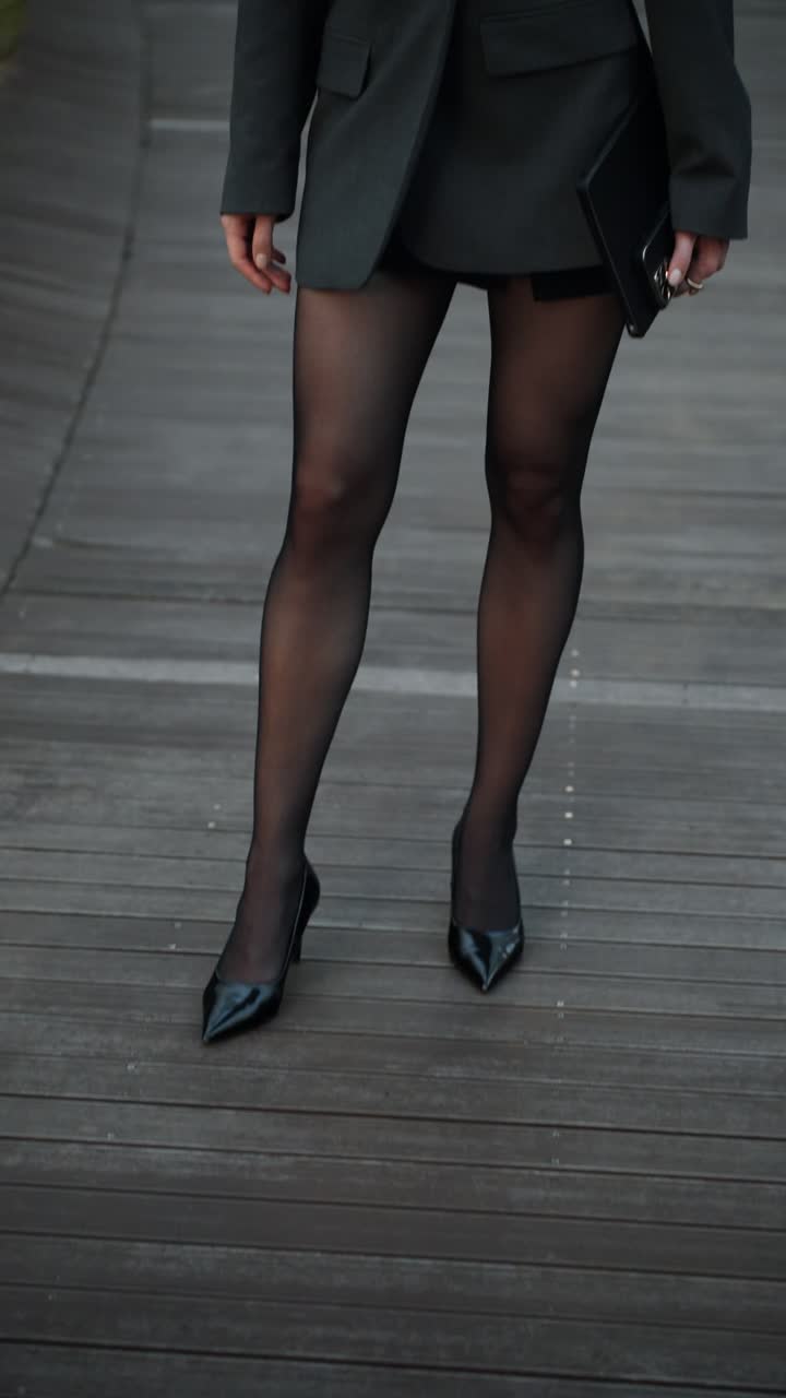 A fashionable Caucasian businesswoman holding a phone and tablet looks at the camera on a Seoul rooftop, her strong, pretty face revealed in a slow tilt-up and push-in shot