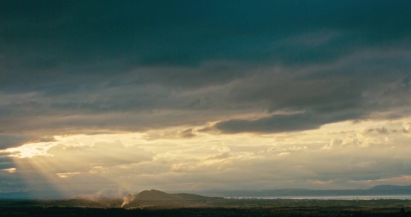 Dramatic storm clouds with sunbeams breaking through onto a distant
landscape. Moody weather scene with atmospheric light, layered clouds,
and panoramic natural scenery.