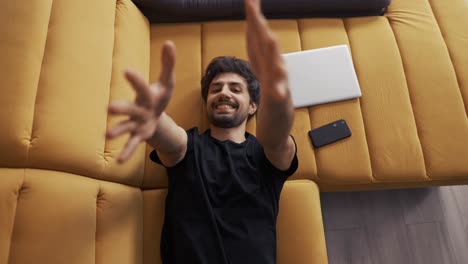 Top-view-of-a-young-man-lying-on-couch-at-home-stretching-hands-to-the-camera