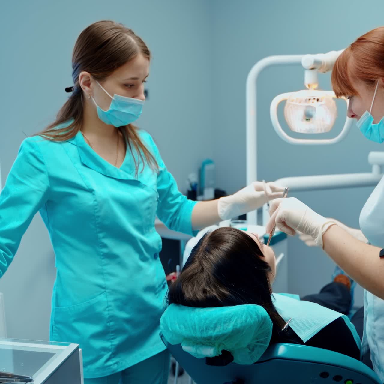 Patient at dentist's office. Female stomatologist together with assistant in medical uniform are treating woman's teeth in modern clinic.