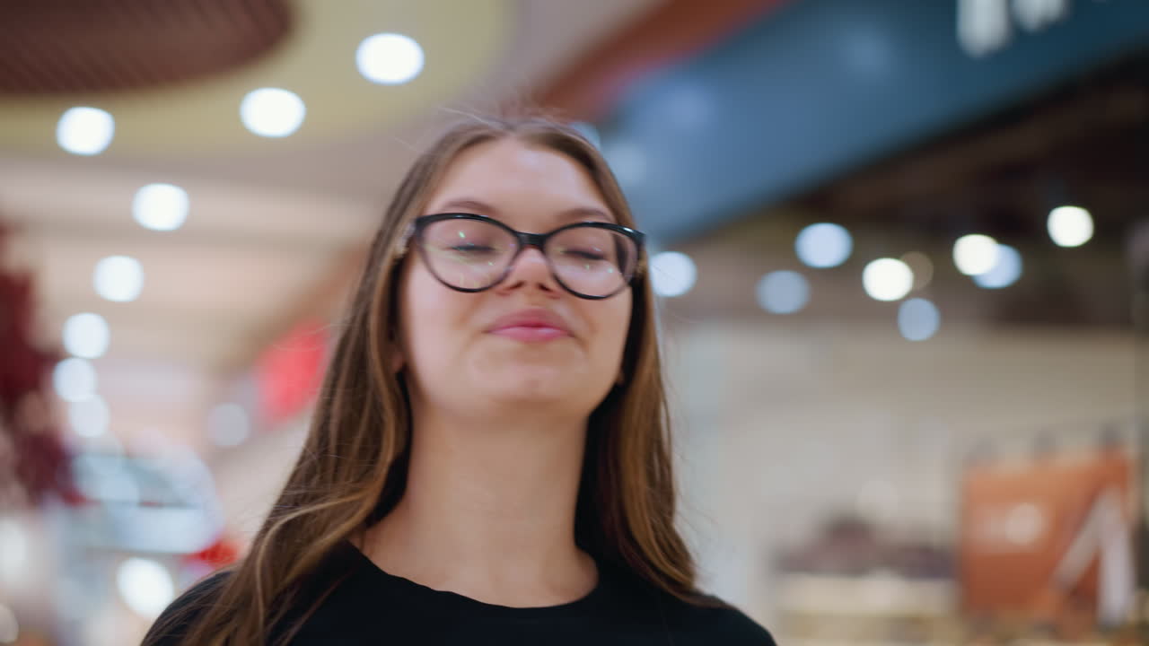 joven con camiseta negra y gafas mirando contemplativa con luces borrosas y estructuras indistintas en el fondo, creando una atmósfera reflexiva y reflexiva