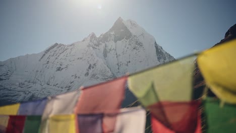 snowcapped mountains and prayer flags in nepal, close up colorful tibetan prayer flags on blue sky sunny day in the sun in the himalayas in annapurna region, colourful buddhism flags in nature