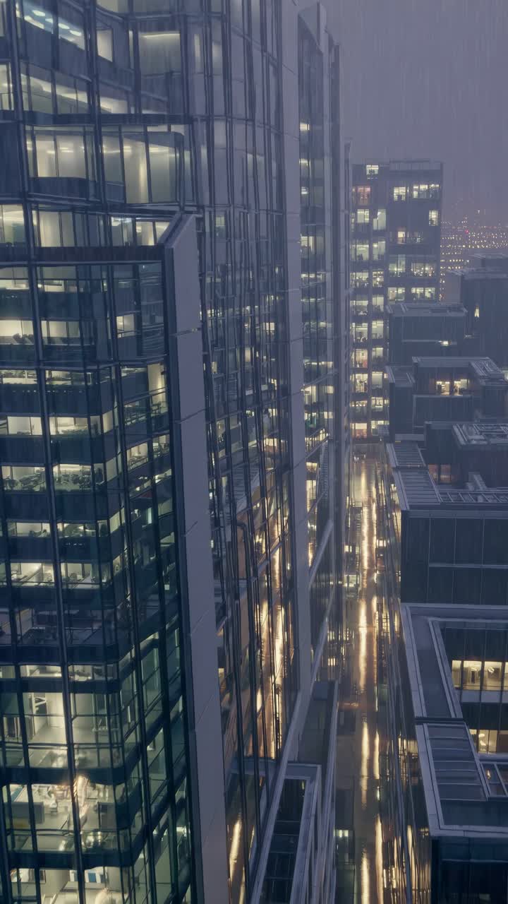 High-angle video frame of modern glass skyscrapers at night, showcasing reflections and city lights