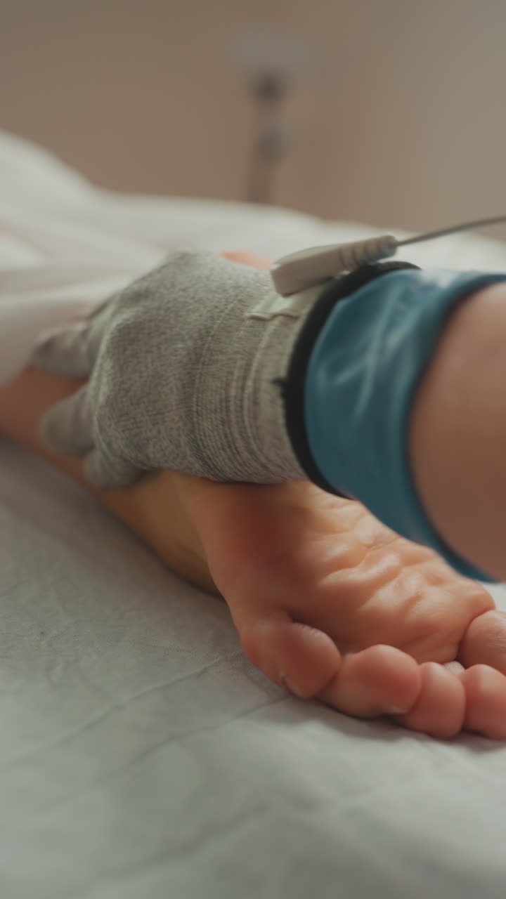 Primo piano di piede nudo che riceve terapia con microcorrente. Operatore con guanti applica elettrodo conduttivo lungo la pianta del piede su un lettino da trattamento bianco. Illuminazione soft da spa, pressione delicata, dettagli visibili della pelle, effetto lenitivo.