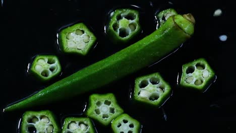 delicious green uncooked okra slices falling onto water surface isolated on black background in slow motion