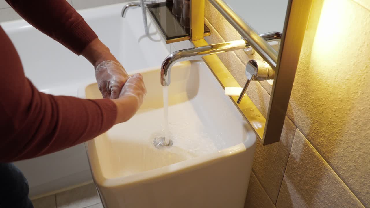 Carefully washing hands in a bathroom sink with soap and hot water - concept: COVID prevention, disease, disinfect, hygiene