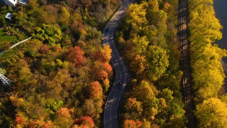 Aerial-shot-of-a-car-driving-on-winding-road-adjacent-to-railway-alongside-Nemunas-River-in-Kaunas,-Lithuania