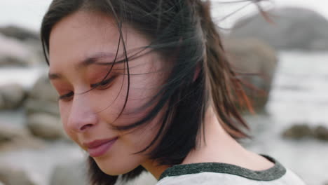 portrait of beautiful asian woman smiling enjoying cloudy seaside exploring vacation lifestyle with wind blowing hair on beach