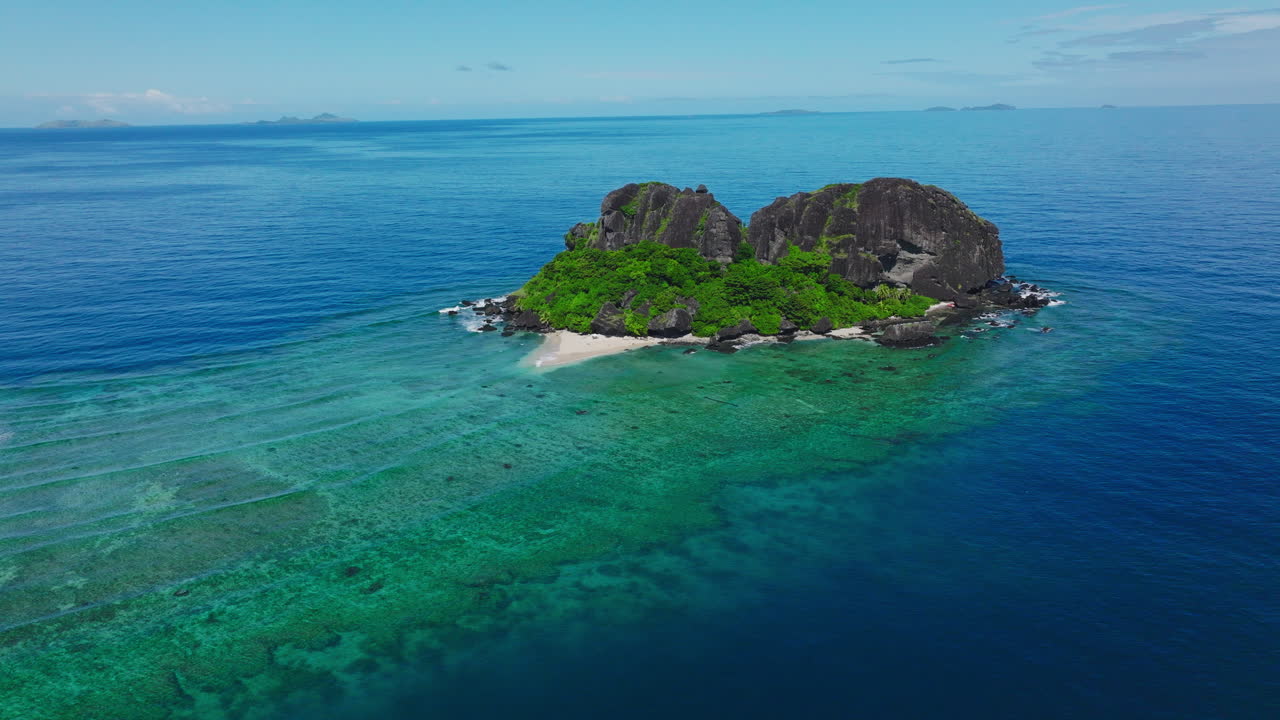 Tropical island in bright blue water with coral reef surrounding it from above
