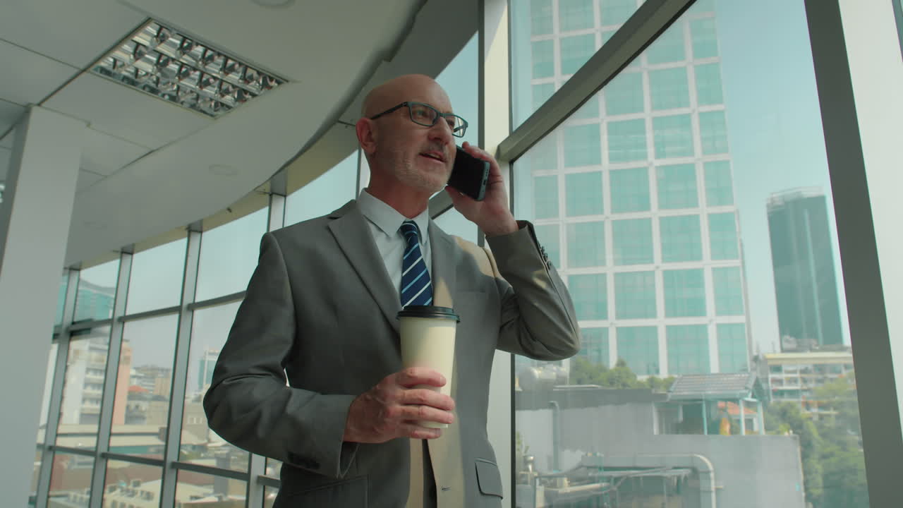 Mature Businessman with Coffee Talking on Smartphone in Office