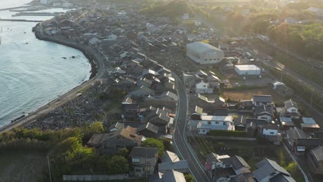 Sunrise-over-Sea-of-Japan-and-small-Mikuriya-Town,-Tottori,-Aerial-Tilt-Shot