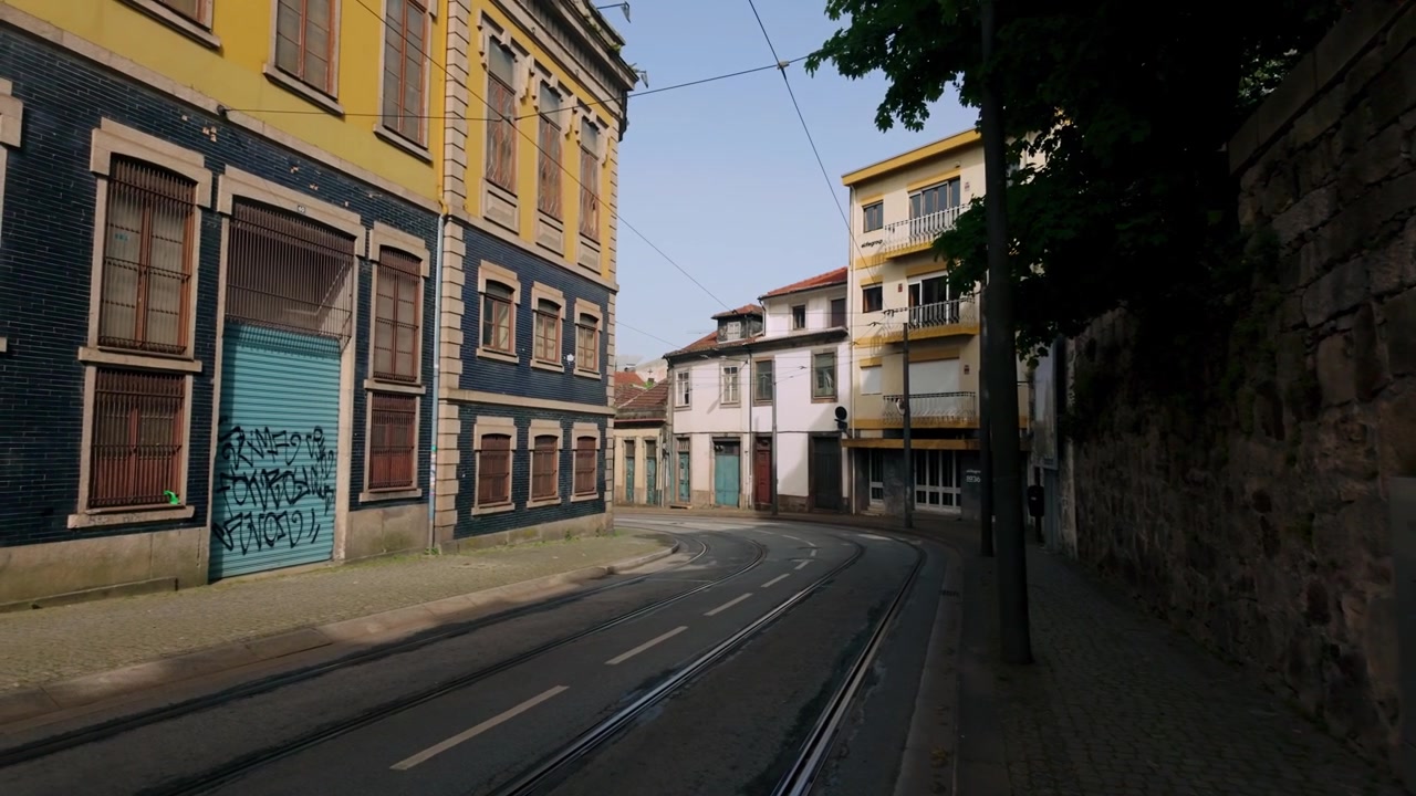 Straathoek in Porto, Portugal, waar tramrails rond oude traditionele gebouwen met kleurrijke gevels en wat stedelijke graffiti buigen. Het gebied is deels in de schaduw, wat contrast biedt.
