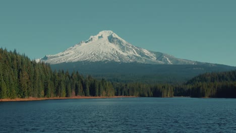 4k-aerial-snowy-mountain-with-lake-and-evergreen-hills-in-foreground-drone-truck-left