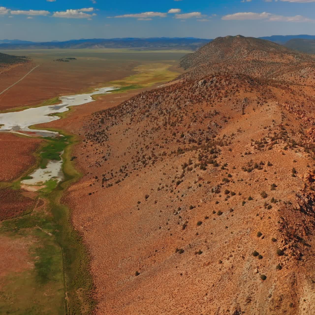 Dry sandy landscape of Nevada, United States on sunny day. Rocky hills with some puddles surrounded by scarce greenery from top view