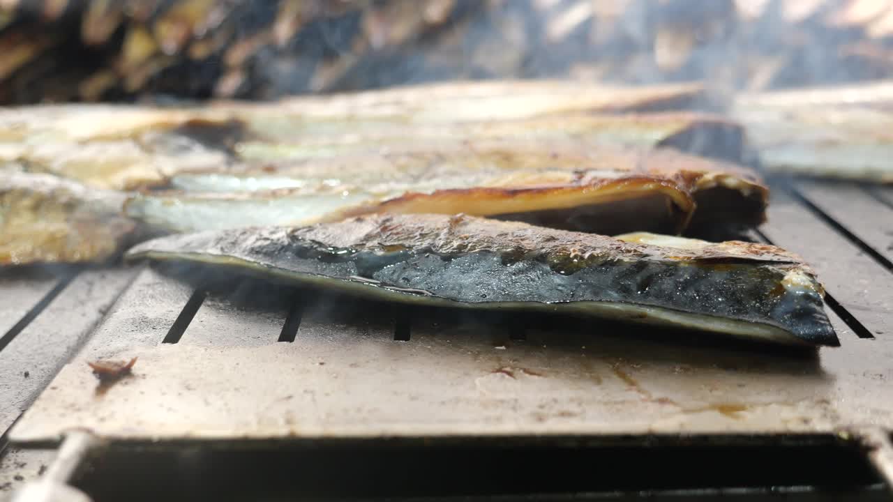 Fish being grilled on a barbecue with smoke rising