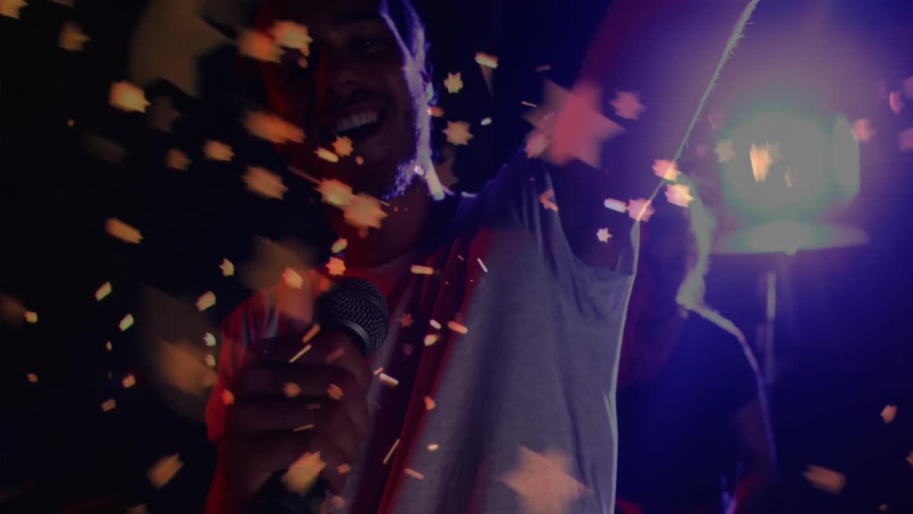 Lead singer grabbing mic causing confetti swirling and spotlight lighting bandmate musician behind