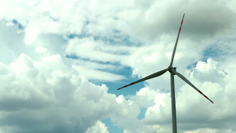 Aerial-footage-showing-a-single-wind-turbine-against-a-backdrop-of-dramatic,-fluffy-clouds-and-a-bright-blue-sky