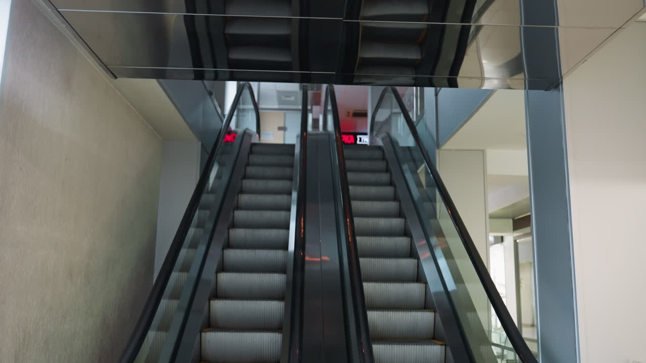 two escalators, one going up and the other coming down, in a modern indoor setting. The camera highlights the sleek design and functionality of the escalators in a well-lit commercial space